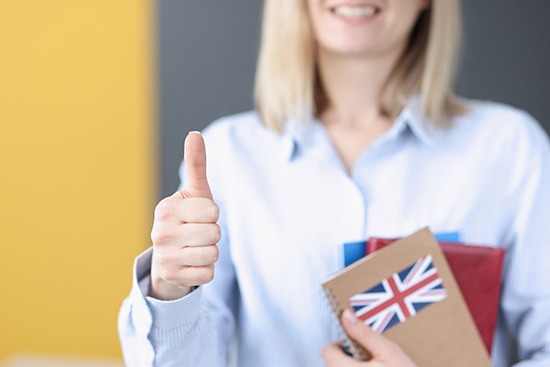 Woman holds textbooks with UK flag and shows thumbs up